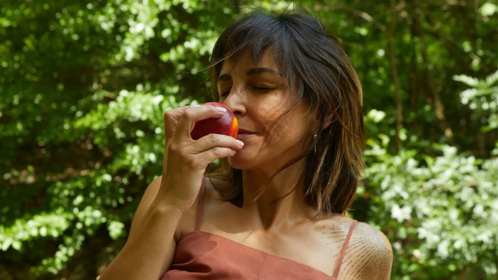 Sonia Morillo oliendo una nectarina, con los ojos cerrados, entre vegetación